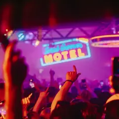Gente bailando bajo el letrero de neón "Solid Grooves Ibiza Motel" en una fiesta vibrante.