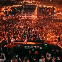 Multitud vibrante en una discoteca, luces naranjas y humo. DJ en el escenario. ¡Una noche de fiesta inolvidable, código 11 octubre!