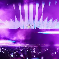 DJ en escenario con luces moradas y público con móviles. Un momento cumbre de la industria de la música.