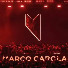 Multitud vibrante en Madrid, luces rojas y el logo de Marco Carola iluminan la noche.