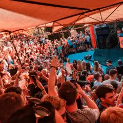 Multitud disfrutando de un concierto de house, género musical que anima la fiesta bajo una carpa naranja.
