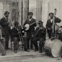 Grupo de músicos tocando jazz años 50: clarinete, trombón, banjo, violín, contrabajo y batería.