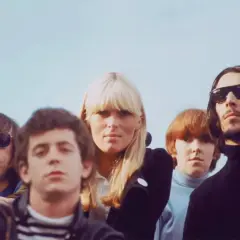 Cinco miembros de The Velvet Underground, pioneros del sonido new wave 80, posan con miradas intensas bajo un cielo azul.