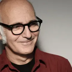 Retrato de Ludovico Einaudi, músico italiano. Su edad se refleja en su mirada serena y su cabello canoso. Viste una camisa roja.