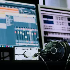 Estudio de **audio digital** con monitores mostrando software de producción musical, un amplificador de auriculares y auriculares negros.