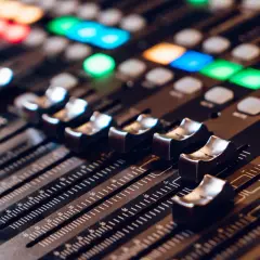 Primer plano de una mesa de mezclas con faders y botones iluminados. La **técnica de sonido** se manifiesta en este panel de control para crear la atmósfera perfecta.
