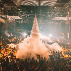 Multitud en un **tardeo techno Madrid**, con humo saliendo del centro y luces que iluminan la fiesta.