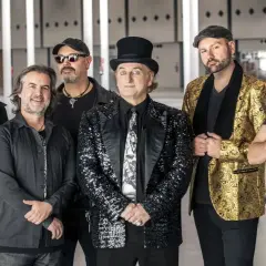 Los miembros de la Orquesta Mondragón posan juntos, listos para un concierto. El cantante principal lleva un sombrero de copa y un traje brillante.