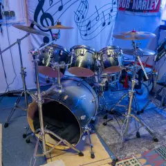 Batería de rock con platillos y un cartel de Bob Marley. ¿Te preguntas dnb que es? Es un género musical.