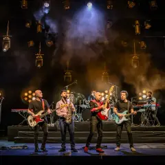 Cinco músicos en el escenario, con guitarras, bajo, saxofón y teclados. La banda, como si fueran hermanos, comparte sus opiniones musicales.