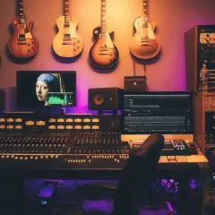 Estudio de grabación con guitarras colgadas, mesa de mezclas, monitores y un ordenador mostrando "La joven de la perla", ideal para samplear.