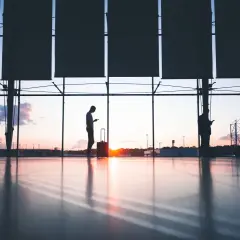 Siluetas de personas con maletas en un aeropuerto al atardecer. Quizás buscando ofertas en **que es ticketswap** para su próximo viaje.