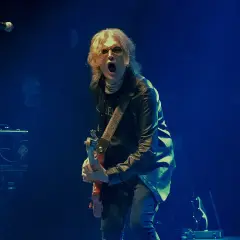 Glenn Hughes, con su banda, desata energía en el escenario. El vocalista y guitarrista, con su icónica melena rubia, grita al público mientras toca su instrumento.
