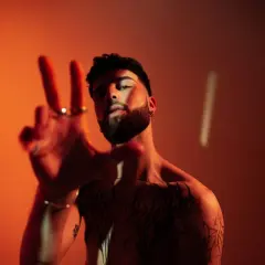Joven con tatuajes y barba hace el signo de la paz. ¿Oguz DJ de dónde es?