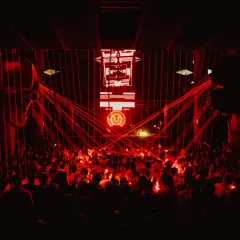 Multitud vibrante en un club nocturno, bañada en luces rojas. El logo de "Circus Nation" ilumina el escenario.