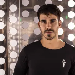 Raúl Pacheco DJ, con su mirada intensa, posa frente a un fondo metálico con círculos luminosos.