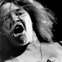 Janis Joplin canta con pasión, su boca abierta y cabello al viento capturan la energía cruda de su voz.