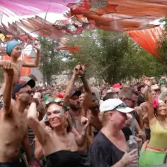 Multitud bailando en un festival psytrance España, con decoraciones coloridas y una estructura de madera.