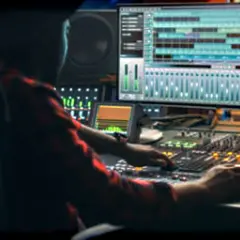 Persona trabajando en una mesa de mezclas, con una pantalla mostrando pistas de audio. Ideal para masterización online gratis.