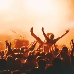 Multitud animada en un concierto, con una persona siendo levantada. La atmósfera naranja sugiere la emoción de los festivales en octubre.