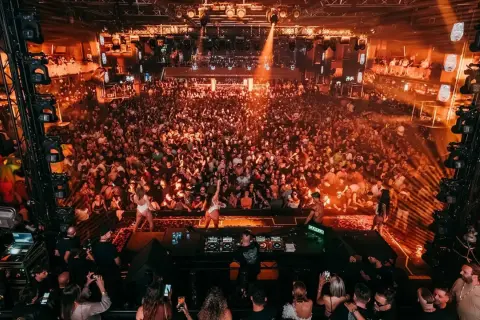 Multitud vibrante en una discoteca, luces naranjas y humo. DJ en el escenario. ¡Una noche de fiesta inolvidable, código 11 octubre!