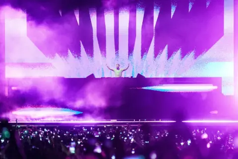 DJ en escenario con luces moradas y público con móviles. Un momento cumbre de la industria de la música.