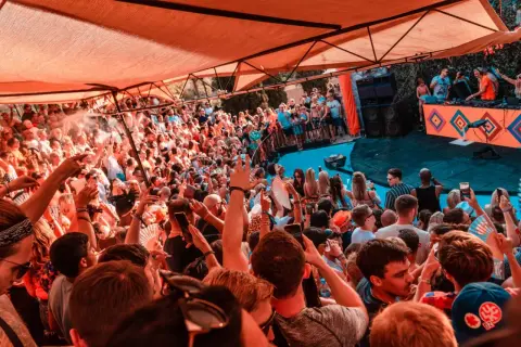 Multitud disfrutando de un concierto de house, género musical que anima la fiesta bajo una carpa naranja.