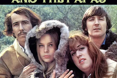 Los miembros de The Mamas & the Papas posan juntos, con un hombre a la izquierda y otro a la derecha, y dos mujeres en el centro.