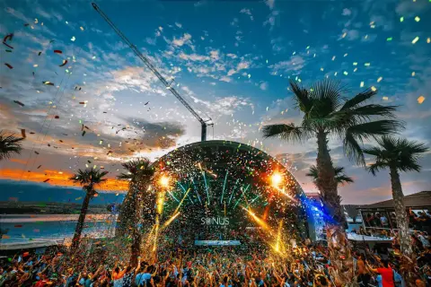 Multitud celebra en el festival croacia techno bajo confeti y luces. Palmeras y grúa completan la escena.