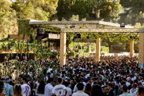 Multitud disfrutando de música electrónica en un evento al aire libre, con una estructura decorada con vegetación. Ambiente festivo en Brunch Electronik Lisboa.