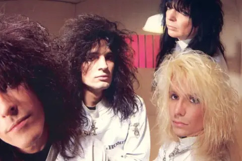 Vince Neil joven y su banda Mötley Crüe posan con sus icónicos peinados y atuendos de glam rock.