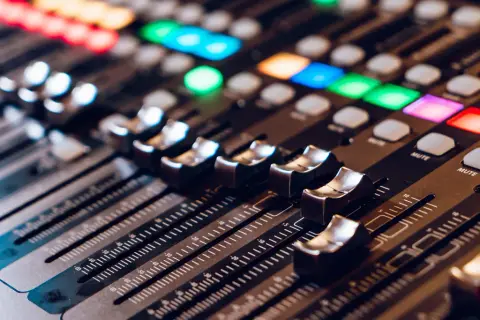 Primer plano de una mesa de mezclas con faders y botones iluminados. La **técnica de sonido** se manifiesta en este panel de control para crear la atmósfera perfecta.