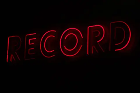 Letrero de neón rojo con la palabra "RECORD", evocando la era dorada de los sellos discográficos y la música.