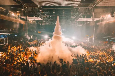 Multitud en un **tardeo techno Madrid**, con humo saliendo del centro y luces que iluminan la fiesta.