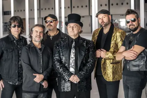 Los miembros de la Orquesta Mondragón posan juntos, listos para un concierto. El cantante principal lleva un sombrero de copa y un traje brillante.
