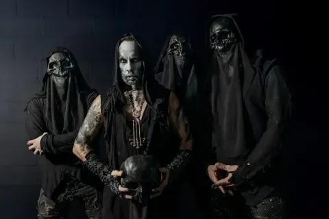 Cuatro figuras encapuchadas, con máscaras de calavera y maquillaje facial pálido, posan sombríamente. El líder sostiene un cráneo, evocando la estética de grupos black metal.