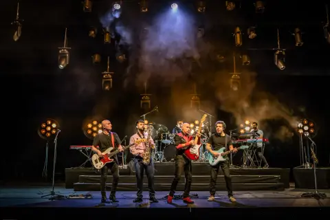 Cinco músicos en el escenario, con guitarras, bajo, saxofón y teclados. La banda, como si fueran hermanos, comparte sus opiniones musicales.