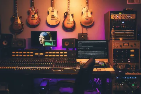 Estudio de grabación con guitarras colgadas, mesa de mezclas, monitores y un ordenador mostrando "La joven de la perla", ideal para samplear.