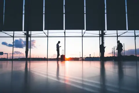 Siluetas de personas con maletas en un aeropuerto al atardecer. Quizás buscando ofertas en **que es ticketswap** para su próximo viaje.