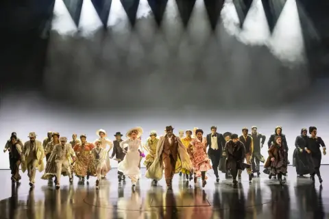 Un grupo diverso de personas corre hacia adelante en un escenario, evocando la energía y el espíritu de "Ragtime, que es".