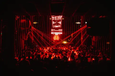 Multitud vibrante en un club nocturno, bañada en luces rojas. El logo de "Circus Nation" ilumina el escenario.
