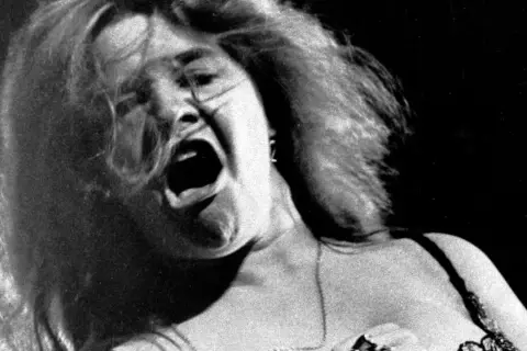 Janis Joplin canta con pasión, su boca abierta y cabello al viento capturan la energía cruda de su voz.