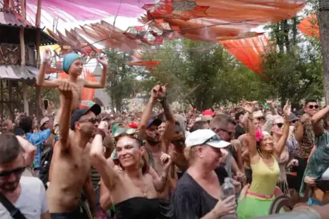 Multitud bailando en un festival psytrance España, con decoraciones coloridas y una estructura de madera.