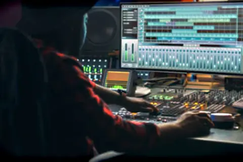 Persona trabajando en una mesa de mezclas, con una pantalla mostrando pistas de audio. Ideal para masterización online gratis.