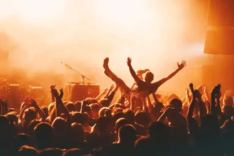 Multitud animada en un concierto, con una persona siendo levantada. La atmósfera naranja sugiere la emoción de los festivales en octubre.