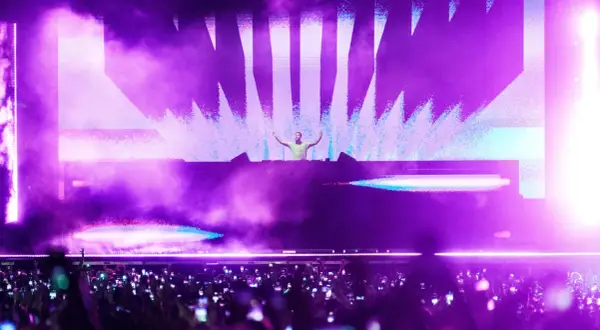 DJ en escenario con luces moradas y público con móviles. Un momento cumbre de la industria de la música.