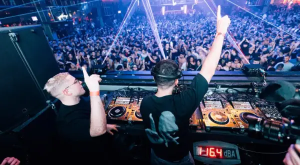 Dos DJs en perfecta alignment, con las manos en alto, animan a una multitud vibrante en una discoteca con luces láser.