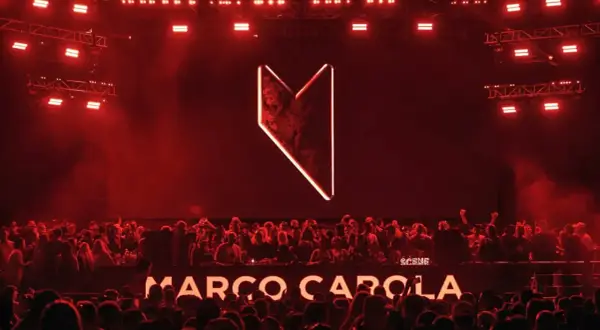Multitud vibrante en Madrid, luces rojas y el logo de Marco Carola iluminan la noche.