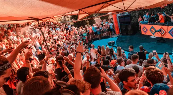 Multitud disfrutando de un concierto de house, género musical que anima la fiesta bajo una carpa naranja.