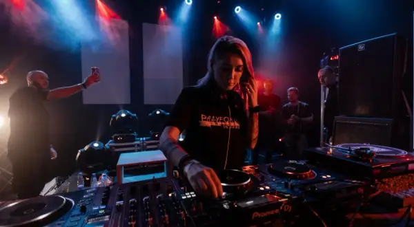 DJ Nusha que es, concentrada en la mesa de mezclas, rodeada de luces y público.